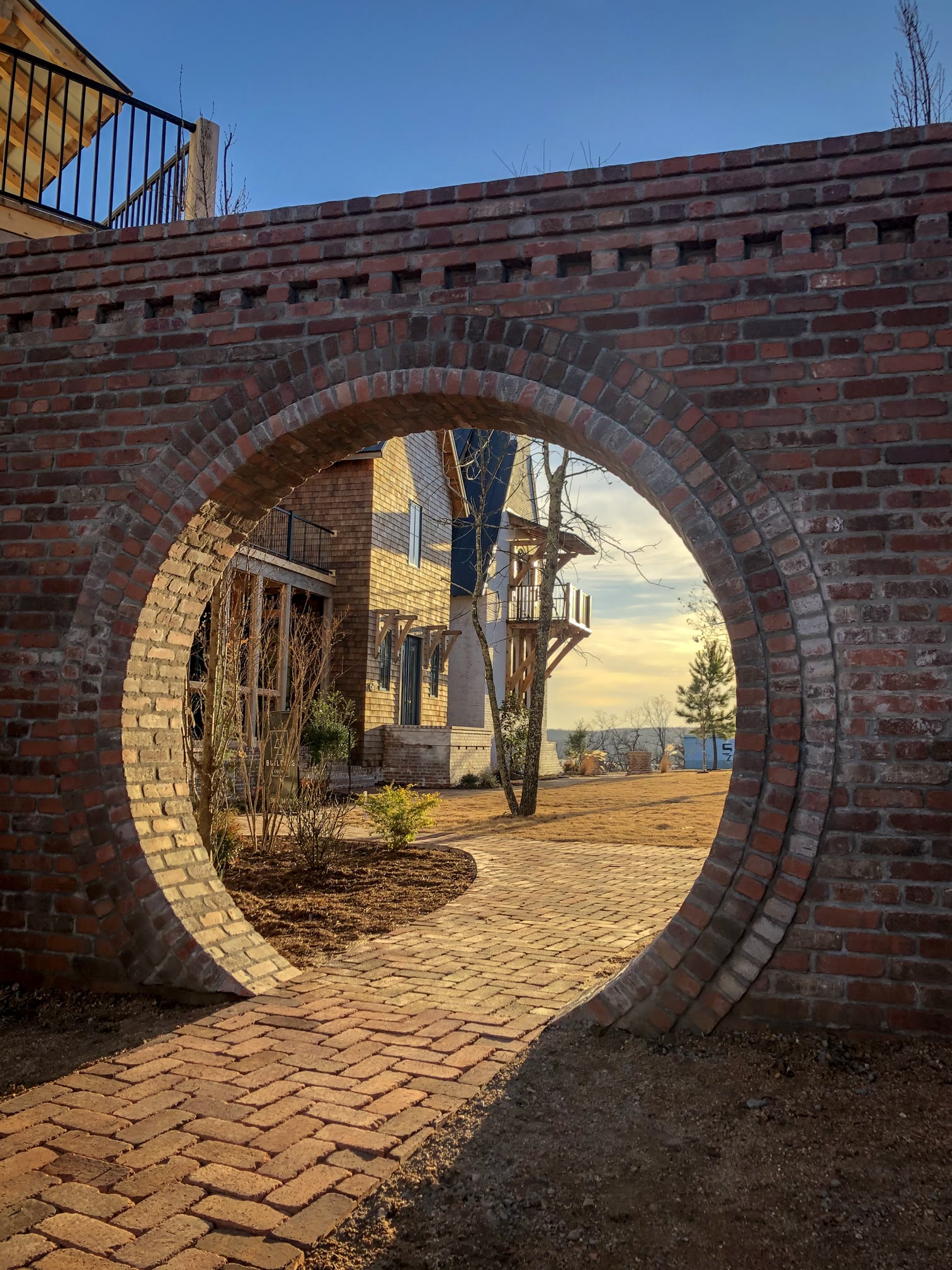 A circular brick moon gate at dusk at The Bend at Carlton Landing, warm sunset light through the opening onto a herringbone brick path