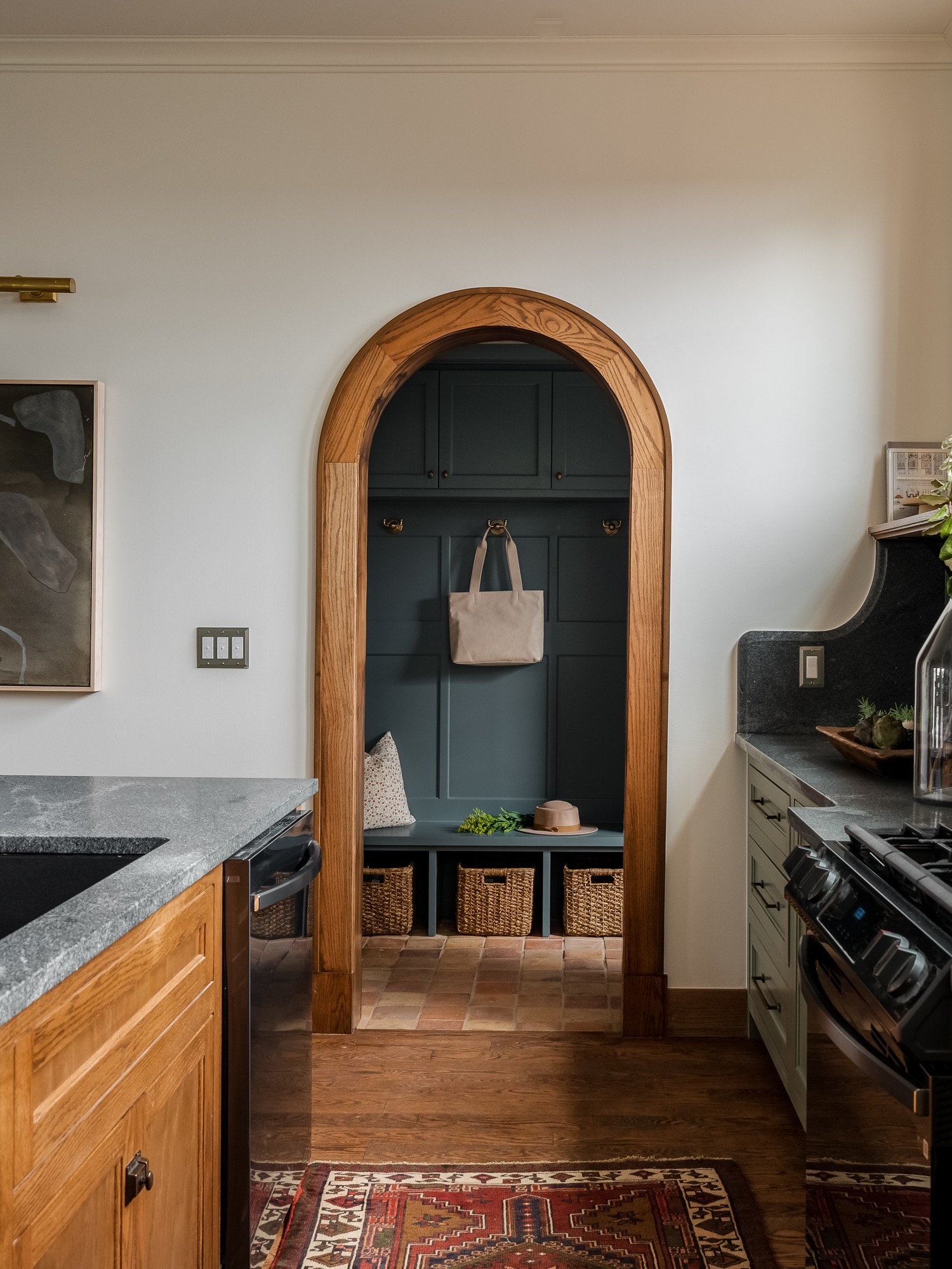 A kitchen interior with an oak-trimmed arched doorway, soapstone counters, and olive cabinetry